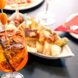 Un bicchiere di spritz aperitivo con amici, ghiaccio e arancia, accompagnato da stuzzichini.