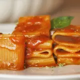 Un primo piatto invitante: paccheri conditi con un sugo rosso vivace, un classico della **pasta allo scarpariello**, guarnito con basilico fresco.