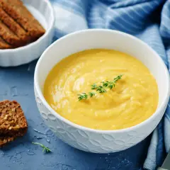 Una ciotola di cremosa salsa di ceci, guarnita con timo, accanto a fette di pane integrale e un tovagliolo blu a righe.