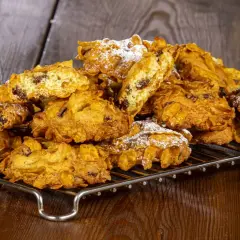 Un mucchio di croccanti biscotti alle corn flakes e uvetta, spolverati di zucchero a velo, sembrano piccole rose del deserto su una griglia.