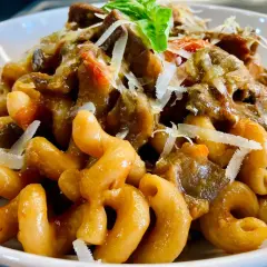 Un piatto invitante di pasta alla norma con melanzane, pomodoro e ricotta salata grattugiata, guarnito con basilico fresco.