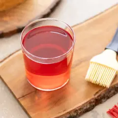 Bagna all'alchermes in un bicchiere, pronta per essere usata con un pennello da cucina su un tagliere di legno.