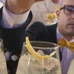 Un barista con papillon giallo prepara un bergamotto spritz, guarnito con scorza di limone.