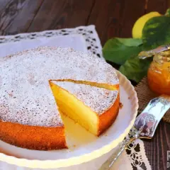 Una soffice torta al limone, spolverata di zucchero a velo, accanto a limoni freschi e marmellata.