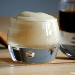 Delizioso zabaione ricetta in un bicchiere, con biscotti e caffè sullo sfondo.