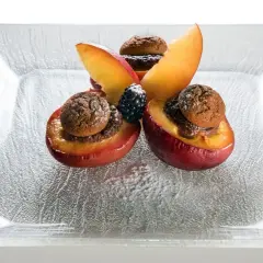 Deliziose pesche ripiene alla piemontese, guarnite con amaretti e frutti di bosco, su un piatto di vetro.