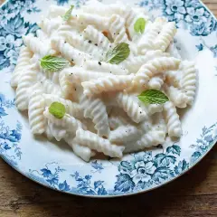 Fusilli cremosi con un sugo leggero alla ricotta, guarniti con foglie di menta fresca su un piatto decorato.