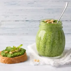 Pesto di rucola ricetta: un vasetto pieno di verde brillante e una bruschetta guarnita, pronti per essere gustati.