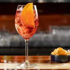Un rinfrescante cocktail spritz, con una fetta d'arancia e ghiaccio, servito su un bancone di legno lucido.