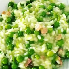 Un cremoso piatto di risi e bisi, con piselli verdi brillanti e cubetti di pancetta croccante, pronto per essere gustato.