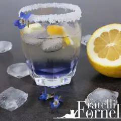 Rinfrescante liquore alla violetta spritz, guarnito con limone e fiori, circondato da cubetti di ghiaccio.