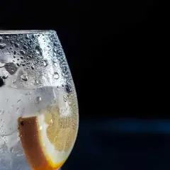 Bicchiere di gin tonic con ghiaccio, bacche di ginepro e fetta d'arancia. La **soda per spritz** rinfrescante crea goccioline sul vetro.