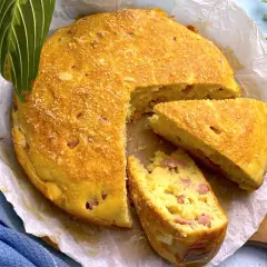 Torta salata prosciutto e formaggio dorata, con una fetta tagliata, su carta da forno.
