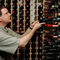 Un uomo sceglie tra una vasta cantina di cru vini, selezionando attentamente una bottiglia.