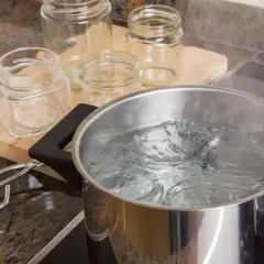 Vapore sale da una pentola piena d'acqua dove si stanno per sterilizzare vasetti pieni. Pinze e altri vasetti vuoti sono sul piano di lavoro.