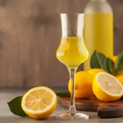 Un bicchiere di limoncello, frutto di un processo di limoncello scientifico, con limoni freschi e una bottiglia sullo sfondo.