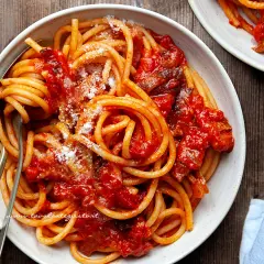 Un piatto invitante di bucatini all'amatriciana ricetta, conditi con sugo rosso e guanciale croccante, spolverati di pecorino.
