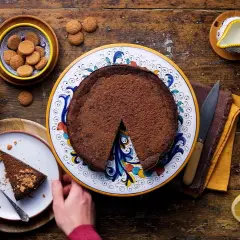 La crescionda spoletina ricetta originale, una torta al cioccolato scuro su un piatto decorato, con amaretti e limoni freschi.