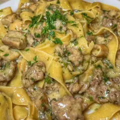 Pappardelle cremose con un saporito sugo di pasta salsiccia e funghi, guarnite con prezzemolo fresco.