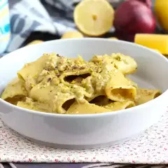 Piatto di pasta tonno e limone, condita con una crema verde e pistacchi tritati, servita in una ciotola bianca.