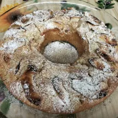 Torta all'acqua soffice e profumata, cosparsa di zucchero a velo, con pezzi di mela visibili.