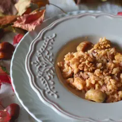 Un cremoso risotto castagne e gorgonzola, guarnito con noci e castagne intere, su un piatto decorato, circondato da foglie autunnali e castagne.