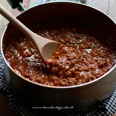 Un pentolino pieno di ragù alla bolognese, pronto per condire la pasta. Un cucchiaio di legno affonda nella salsa densa e profumata.