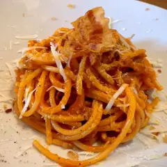 Spaghetti all'amatriciana, un classico piatto romano, perfetto con un vino rosso corposo. Guarnito con guanciale croccante e pecorino.
