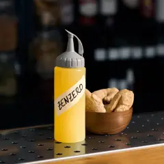 Flacone giallo con etichetta "ZENZERO" e una ciotola di radici di zenzero essiccate.