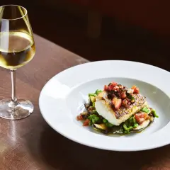 Piatto di pesce con verdure e un bicchiere di vino bianco, perfetti abbinamenti per una ribolla gialla.