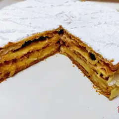 Una deliziosa torta millefoglie con strati di pasta sfoglia croccante e crema pasticcera, cosparsa di zucchero a velo e mandorle.
