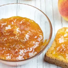 Una ciotola di marmellata di pesche fatta in casa e una fetta biscottata imburrata con la stessa deliziosa marmellata.