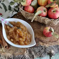 Una ciotola di composta di mele, profumata con cannella e anice stellato, perfetta per la marmellata di natale. Mele rosse in un cesto sullo sfondo.