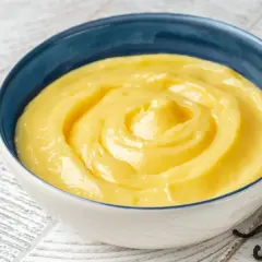 Una ciotola blu piena di soffice crema pasticcera, con baccelli di vaniglia scuri accanto.