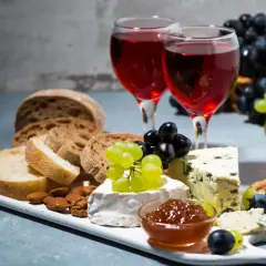 Due calici di rosato vino accompagnano un tagliere con pane, formaggi, uva e frutta secca.