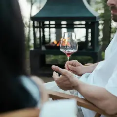Uomo con barba tiene un calice di vino rosso, mostrando come si tiene il calice di vino per il gambo, vicino a un braciere acceso.