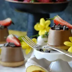 Mini cheesecake al cioccolato con fragola e riccioli di cioccolato, decorati con fiori gialli.
