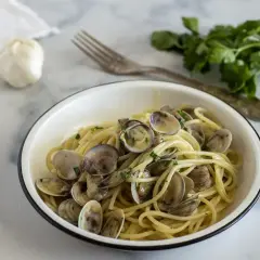 Un piatto invitante di spaghetti alle vongole, con aglio e prezzemolo freschi sullo sfondo.