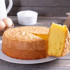 Un soffice pan di spagna, pronto per essere inzuppato con una bagna per pan di spagna. Ingredienti base come uova e zucchero sono visibili.