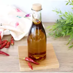 Una bottiglia di olio al peperoncino, con peperoncini rossi secchi sparsi intorno e un tocco di verde sullo sfondo.