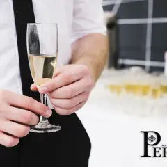 Un bicchiere di prosecco vino dorato, tenuto da mani eleganti, con una piramide di calici sullo sfondo.