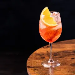 Un bicchiere di spritz Italia, rinfrescante e colorato, con una fetta d'arancia, su un tavolo di legno.