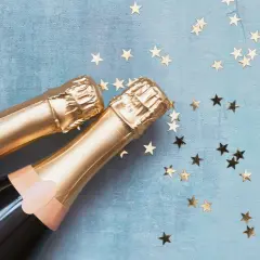 Due bottiglie di spumante dorato su sfondo blu con stelle dorate. Una celebrazione che fa pensare alla differenza tra prosecco e spumante.