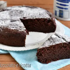 Una deliziosa torta al cioccolato e ricotta, cosparsa di zucchero a velo, con una fetta servita su un tovagliolo azzurro.