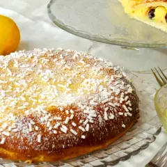 Una deliziosa polacca aversana, cosparsa di zucchero a velo e confettini, accanto a limoni freschi e crema pasticcera.