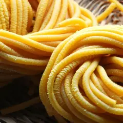Pici all'aglione, pasta fresca fatta a mano, arrotolata in un cesto di vimini, pronta per essere gustata.