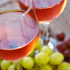 Due calici di vino rosato, frutto della vinificazione in rosato, con grappoli d'uva verde e rossa sullo sfondo.