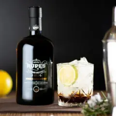 Bottiglia di amaro Rupes, un classico tra gli amari calabresi, accanto a un bicchiere con ghiaccio, lime e un cocktail.