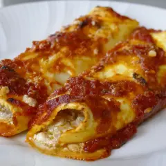 Due cannelloni ripieni, ricoperti di sugo rosso e formaggio, pronti per essere gustati.