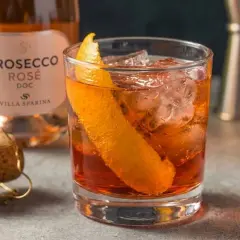 Un Negroni Sbagliato con Prosecco Rosé, guarnito con scorza d'arancia, ghiaccio e una bottiglia di Prosecco Villa Sparina sullo sfondo.